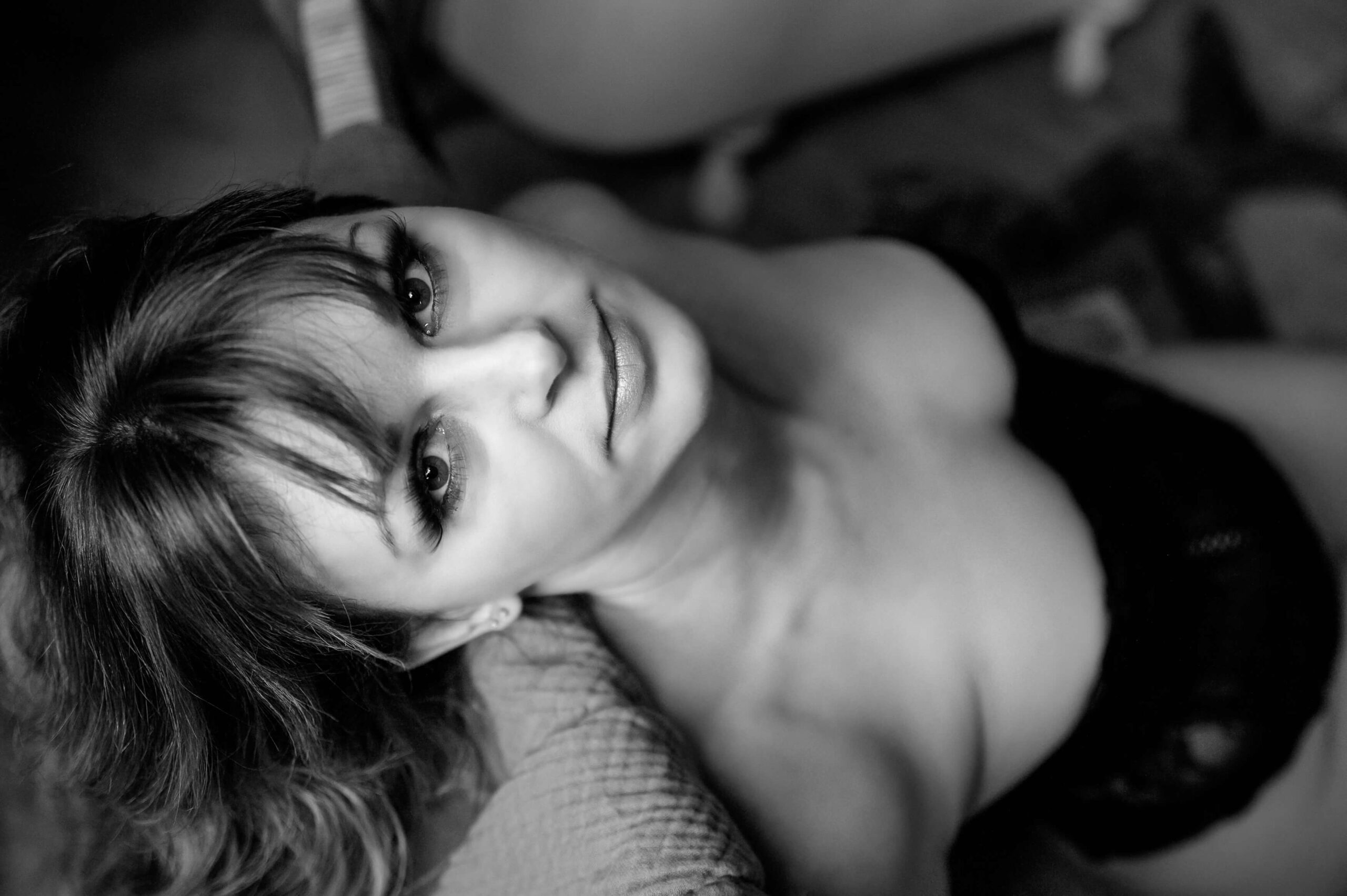Black and white photo of a woman sitting down looking up at the camera for her Ontario Boudoir Photography session.