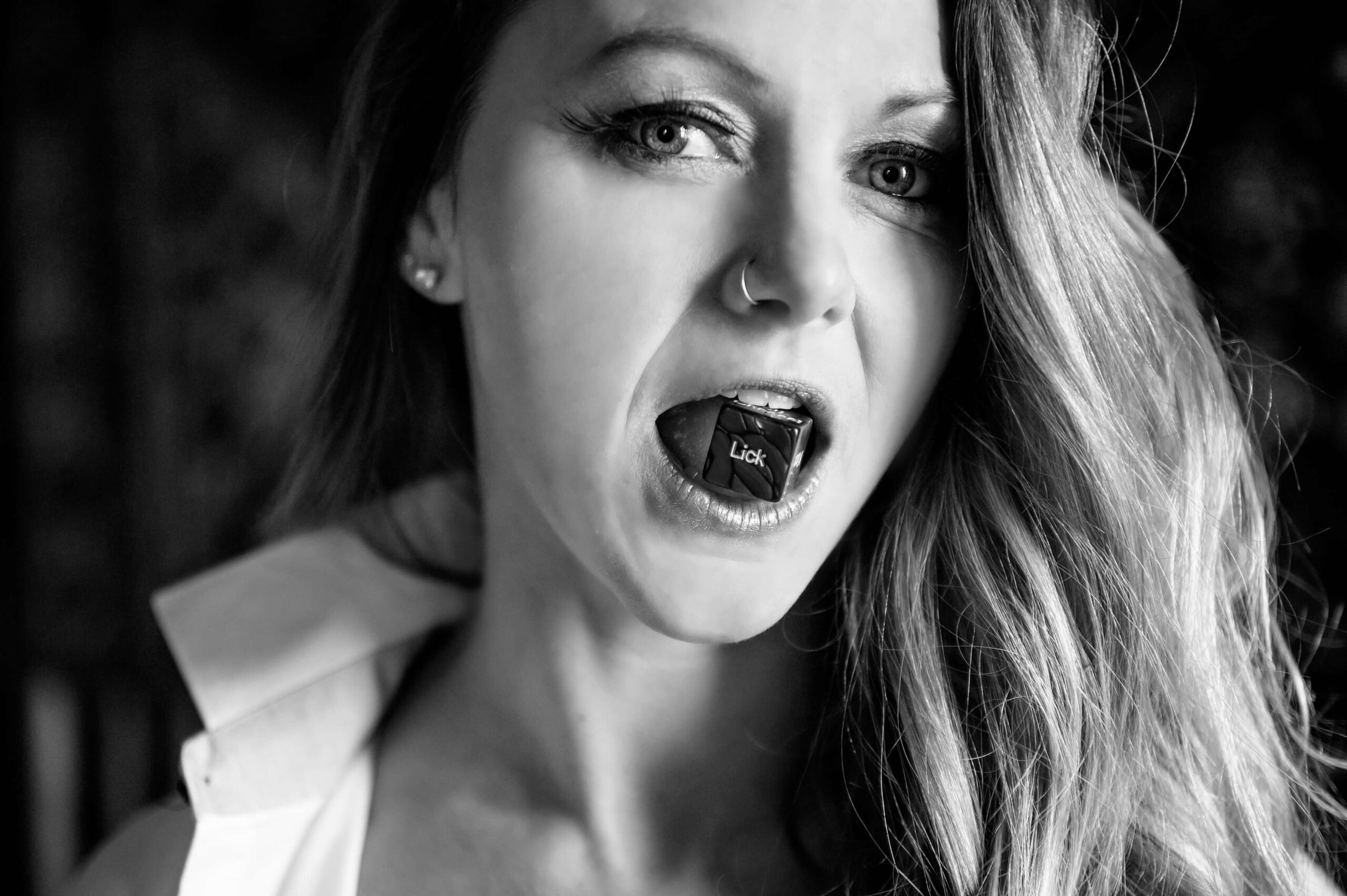 Black and white photo of a woman with a dice in her mouth for her Hamilton Boudoir photography session.