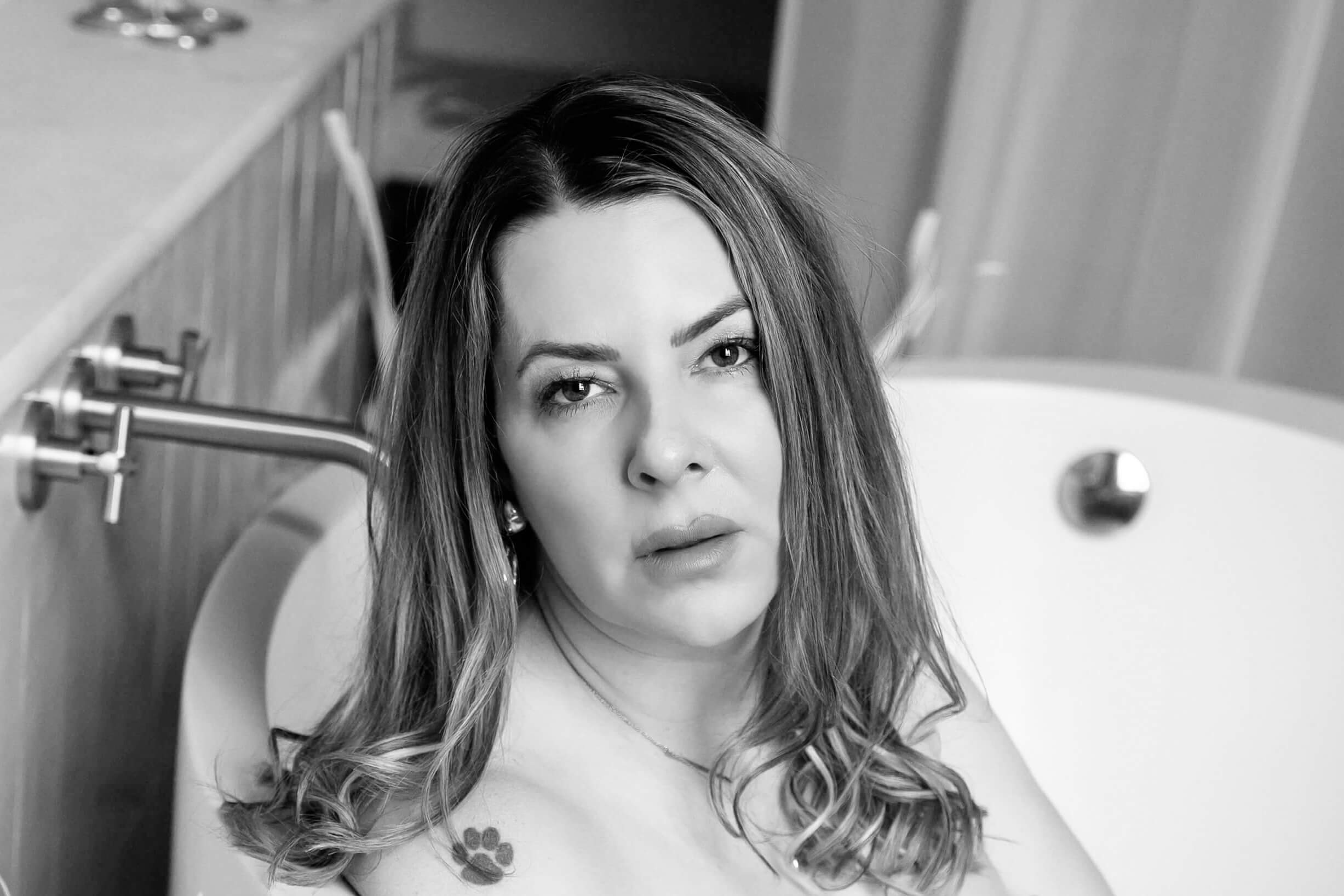 Black and white photo of a woman in a bathtub with a paw print tattoo on her shoulder for her Toronto Boudoir photography session.