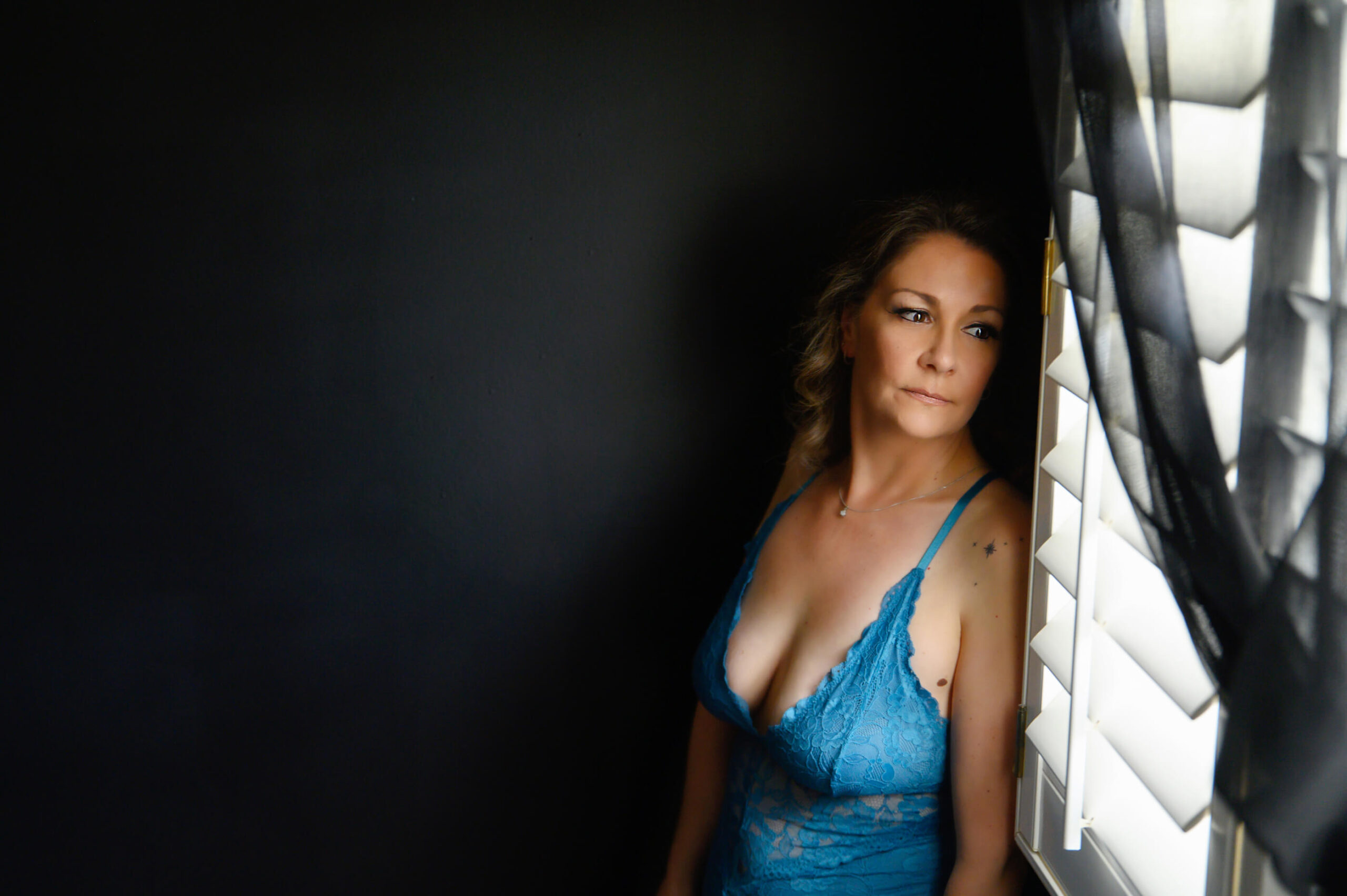 Woman wearing a blue bodysuit looking out a window for her Burlington Boudoir photos.