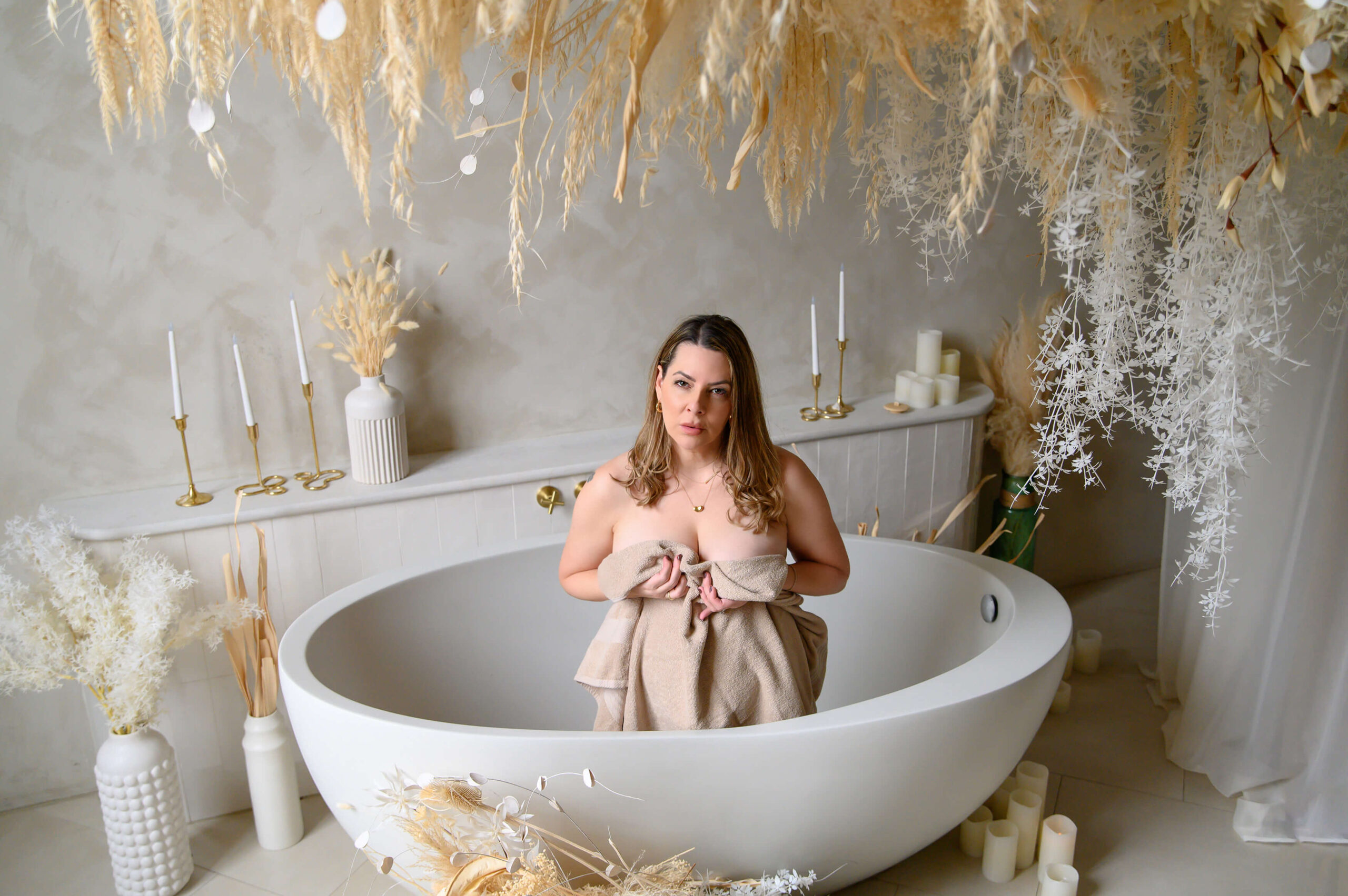 woman holding a beige towel sitting in a bathtub with pampas all around