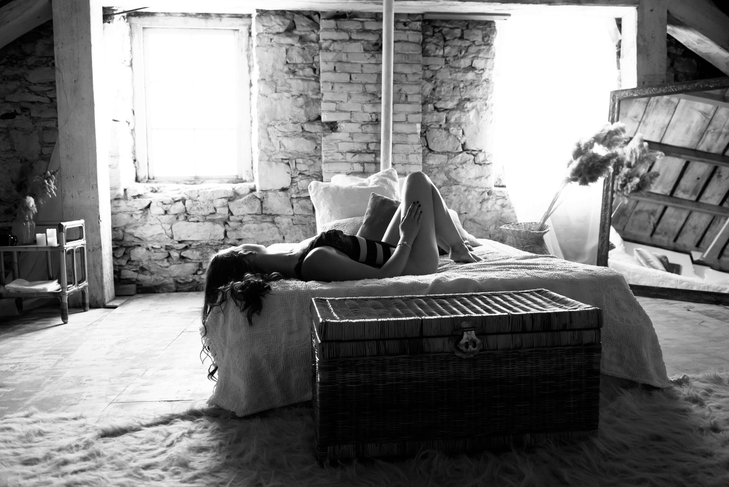 Black and white photo of a woman laying on a bed in black lingerie for her Hamilton boudoir photo session.