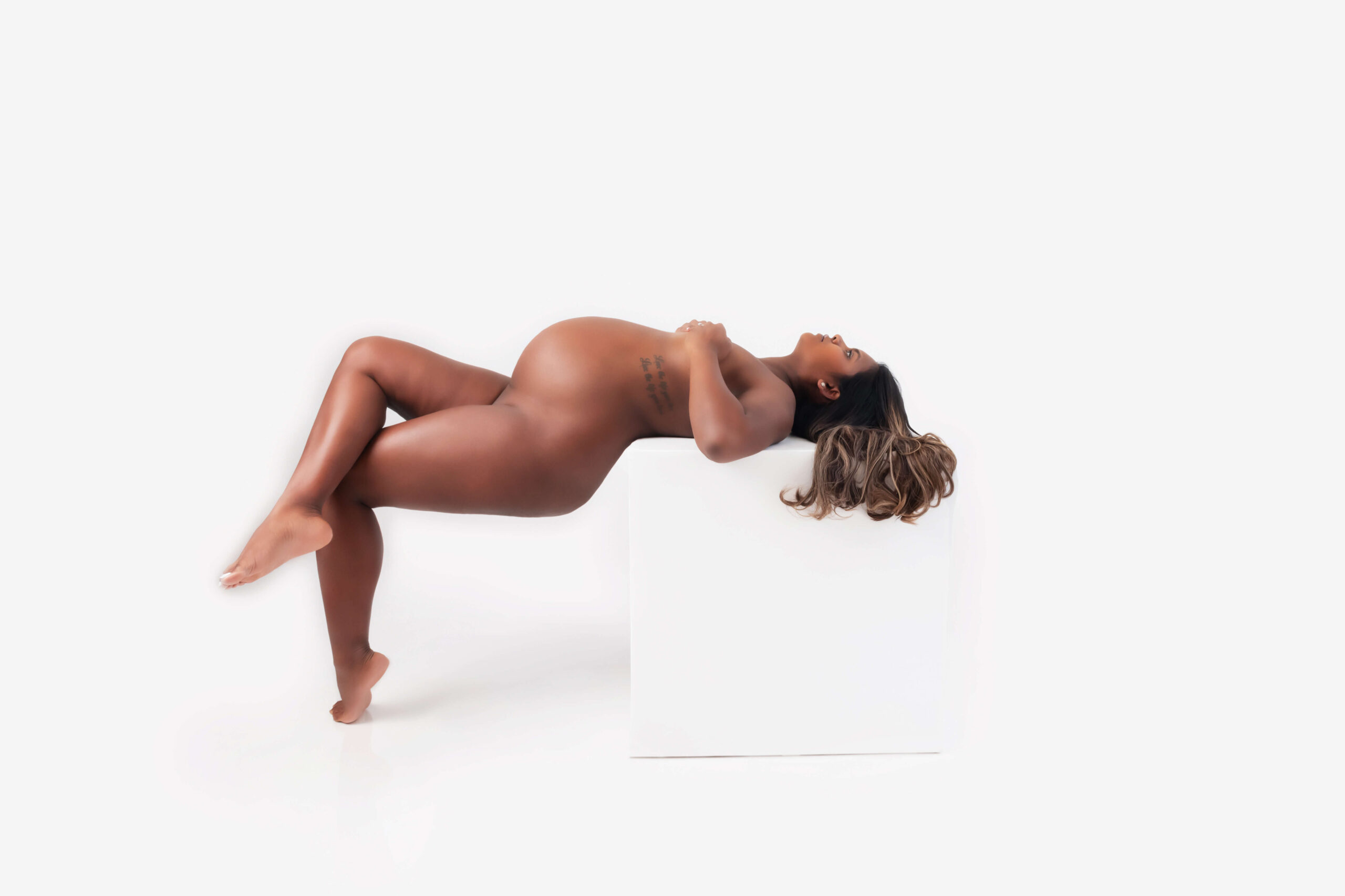 African American pregnant woman naked leaning against a white box for her Boudoir Maternity Photography Session Toronto Ontario.