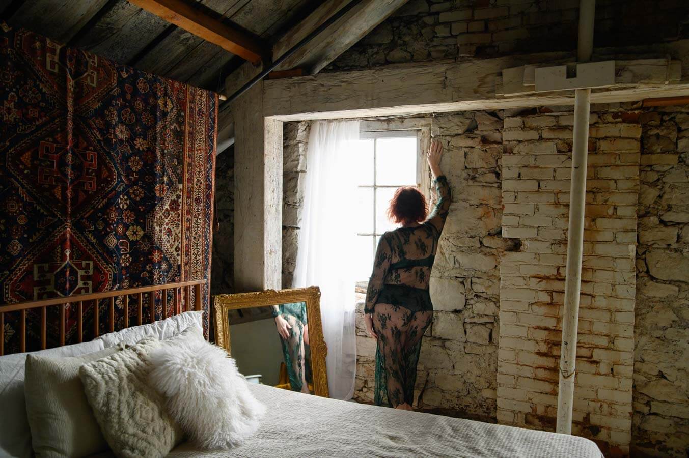 Red-haired woman standing with her hand on a brick wall looking outside for her Hamilton boudoir photos