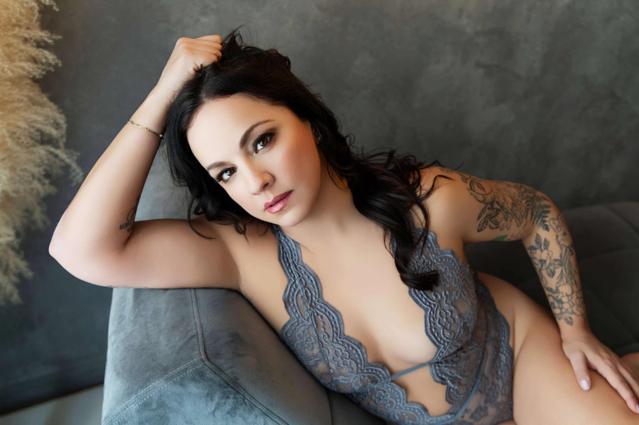brown haired woman sitting on a chaise in a grey bodysuit for her photography session in Burlington, Ontario.